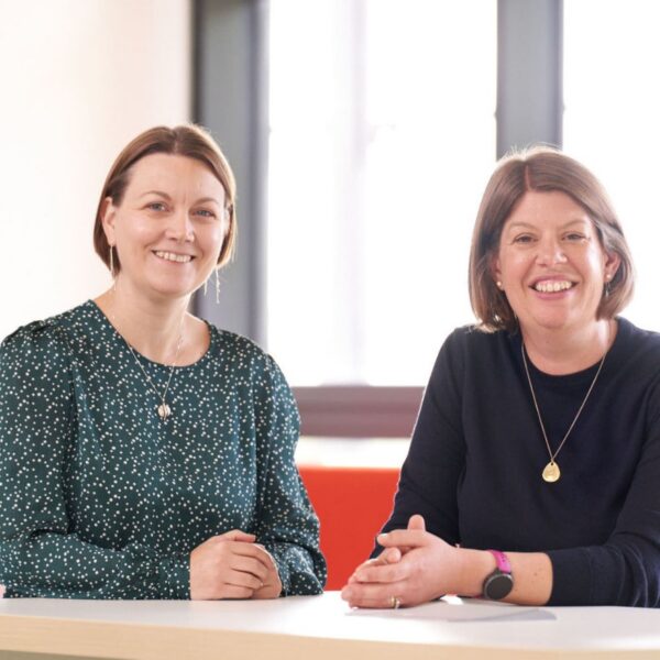 Davinia and Carol sat at a desk, smiling to camera.